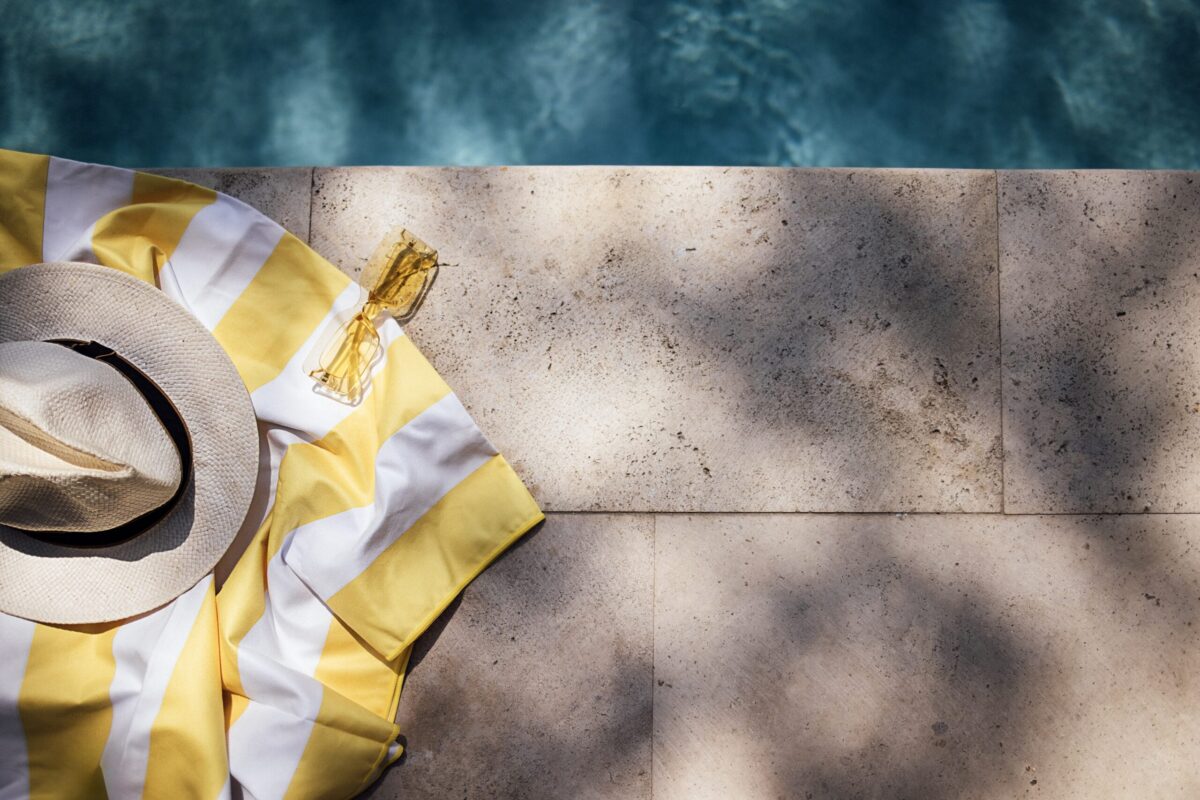 pool deck with yellow and white striped t-shirt and sun hat placed by the side of the pool, shadows from trees