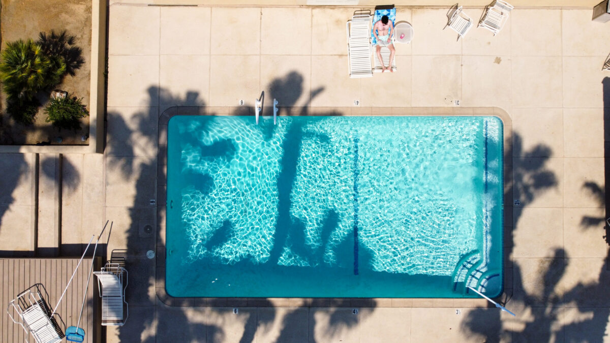 overhead view of man sitting on a deck chair next to a rectangle shaped pool